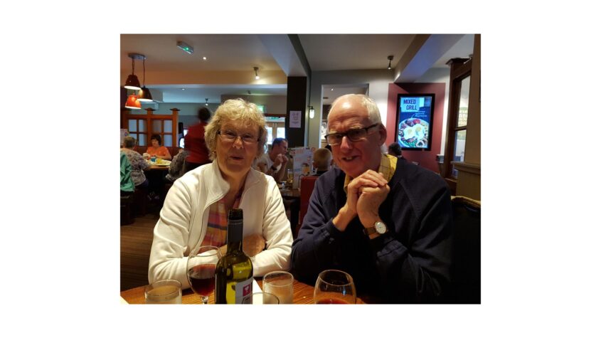 older man and woman sitting at table in restaurant smiling to camera