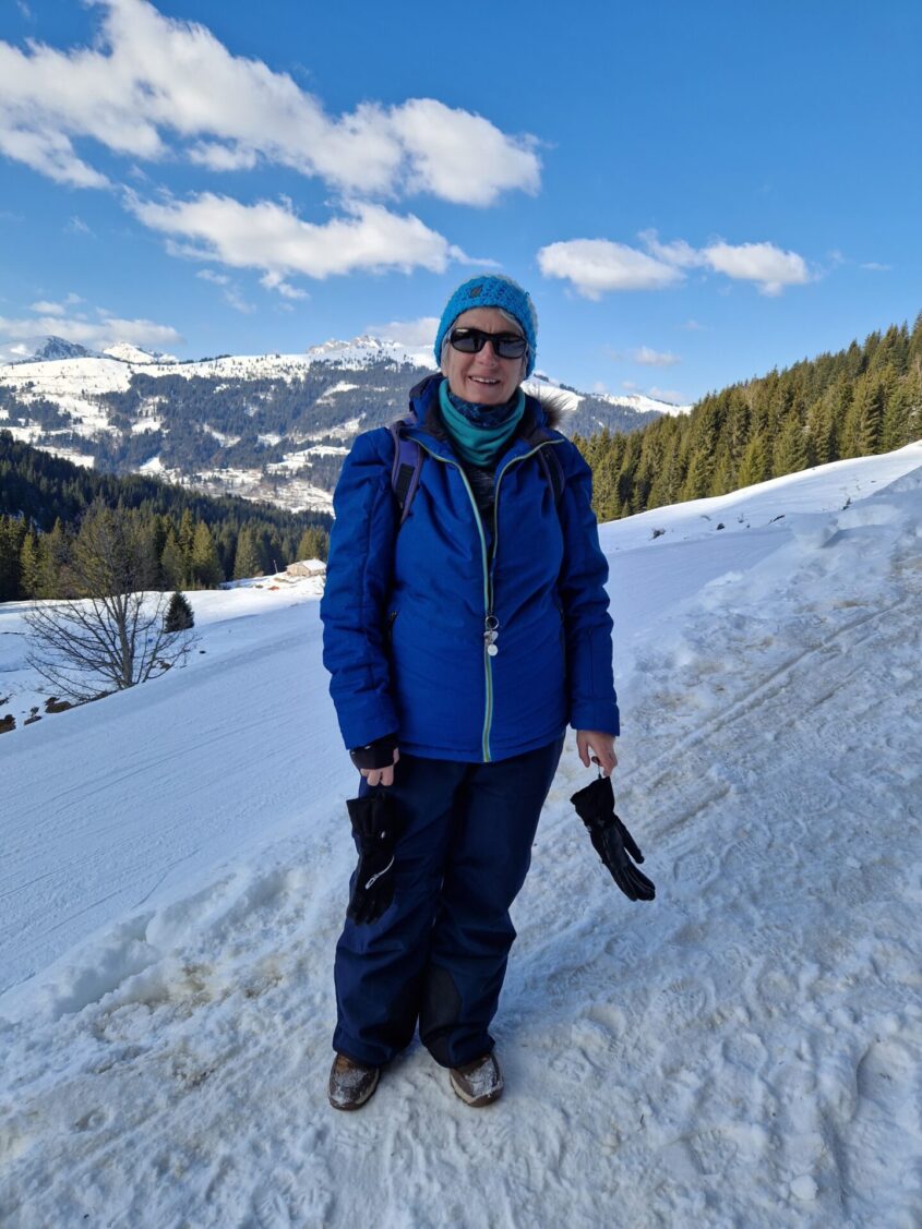 woman standing on a snowy hillside, wearing outdoor gear, hat and sunglasses