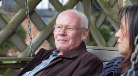 Older man sat on a park bench with a female