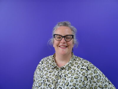 Woman with glasses smiling to camera against purple background