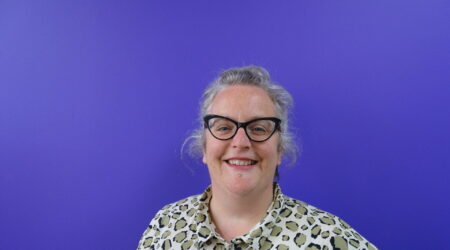 Woman with glasses smiling to camera against purple background