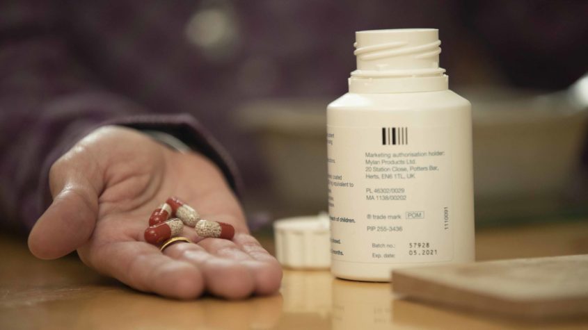 A hand holding pancreatic enzyme replacement capsules.