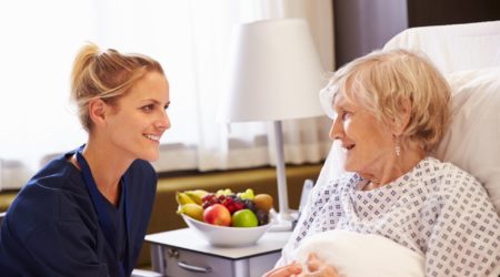 Nurse talking to older female patient in a hospital bed