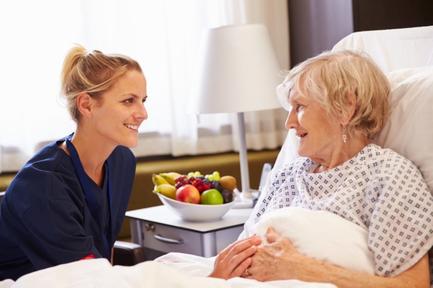 Nurse talking to older female patient in a hospital bed