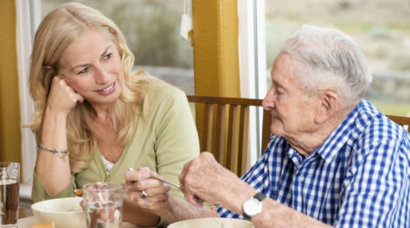 A man and a woman sit at a table talking while the man eats soup.