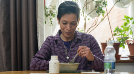 A woman sits at a table to eat a meal alongside her pancreatic enzyme replacement therapy capsules.
