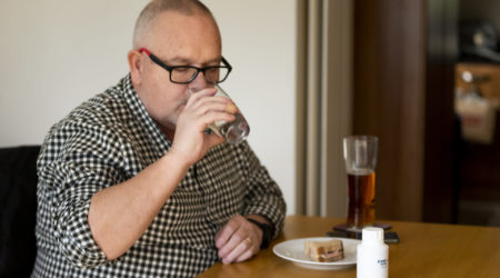 A man sips water as he takes pancreatic enzymes replacement therapy capsules.