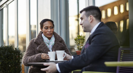 Woman sat outside with a cup of coffee, talking to her friend