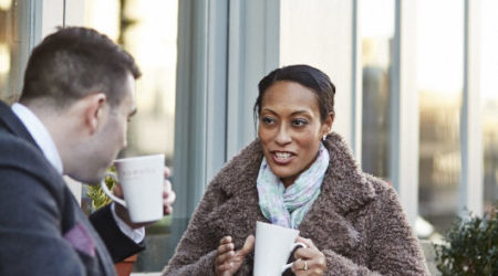 Woman sat outside with a cup of coffee, talking to her friend