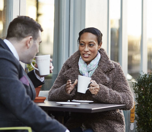 Woman sat outside with a cup of coffee, talking to her friend