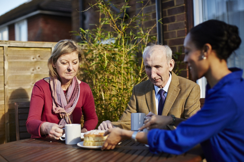 2 women and a man sat in the garden, having tea and cake