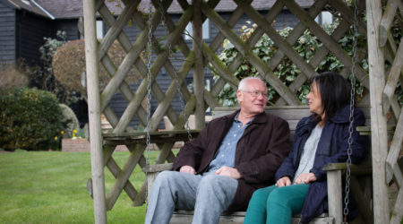 A couple sit on a garden bench together.