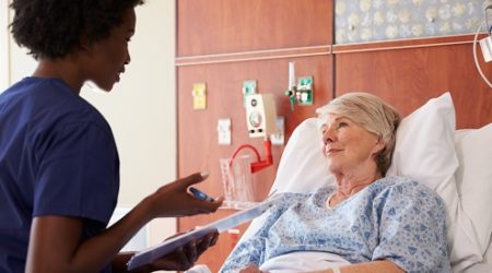 older woman lying in hosptial bed talking to healthcare professional