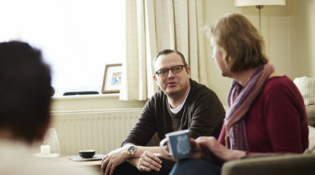 A man and lady talking in the front room, lady holding a cup of tea