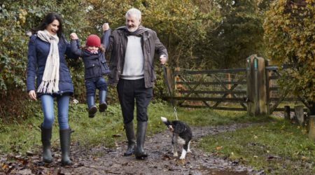 Multi Generation Family Take Dog For Walk In Fall Landscape