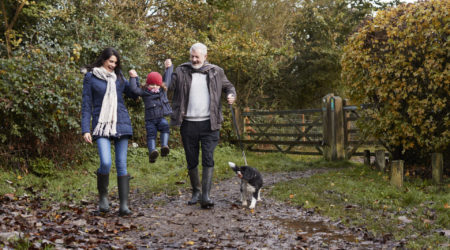 Multi Generation Family Take Dog For Walk In Fall Landscape