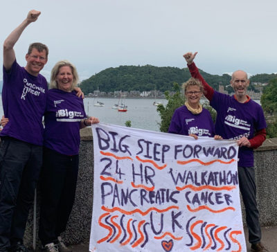 Four people holding a fabric flag for pancreatic cancer UK