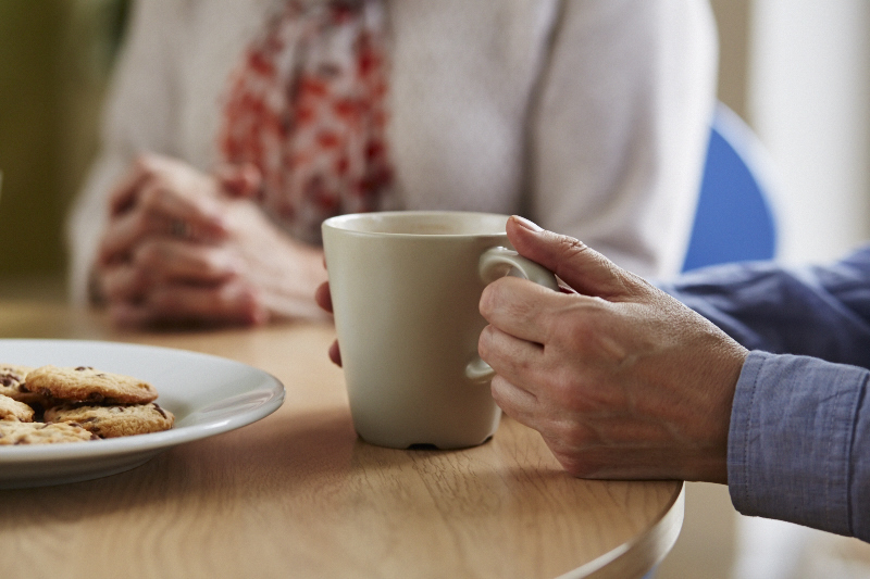 Two people sat at a table, with one person holding their cup of tea