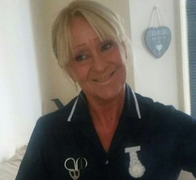 A blonde woman, Sharon, is shown smiling and in her carer's uniform.