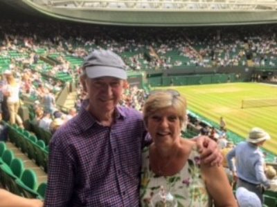 A man and woman smile at the camera in a sunny image taken in the stands of Wimbledon Centre Court