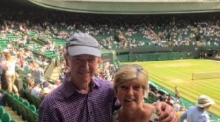 A man and woman smile at the camera in a sunny image taken in the stands of Wimbledon Centre Court