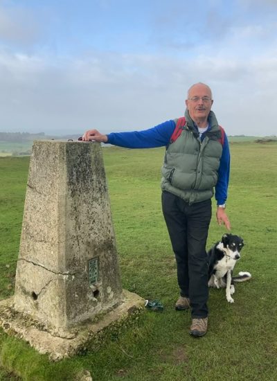 Iain and his dog pose next to a Trig point