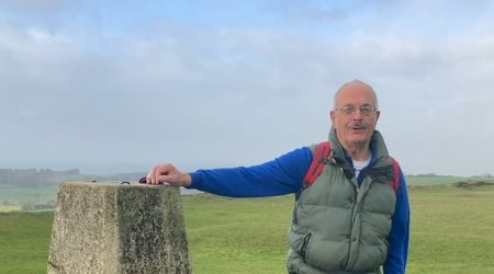 Iain and his dog pose next to a Trig point