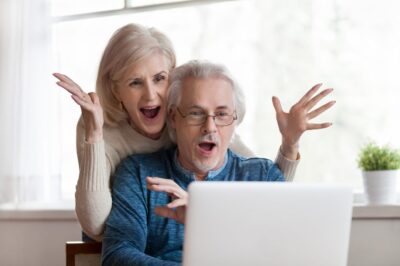 A couple in front of a laptop with their hands in the air in shocked celebration