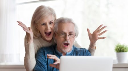 A couple in front of a laptop with their hands in the air in shocked celebration