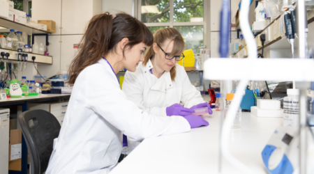 Two researchers working together in a lab wearing their white lab coats