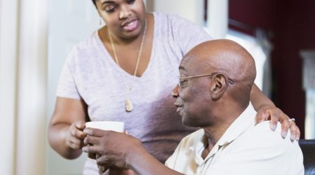 A woman in her 30s getting a cup of coffee for her father, a man in his 60s sitting at a table.