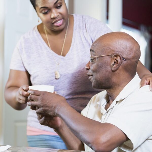 A woman in her 30s getting a cup of coffee for her father, a man in his 60s sitting at a table.