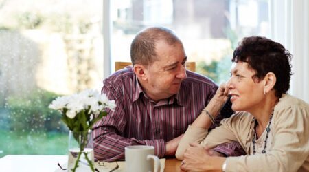 A couple sit at a table holding hands as the talk to each other.