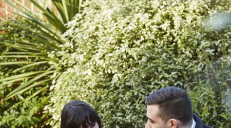 A young man and young woman talk as they sit at a table in a garden