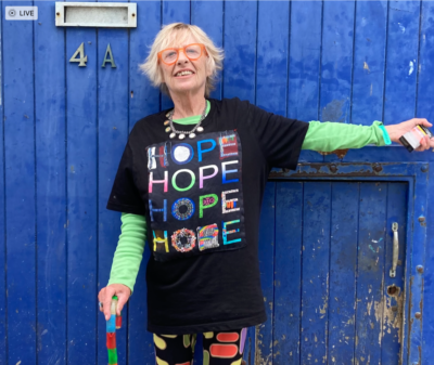 A photo of Jane Travers standing against a blue door wearing a t-shirt with the word hope repeated