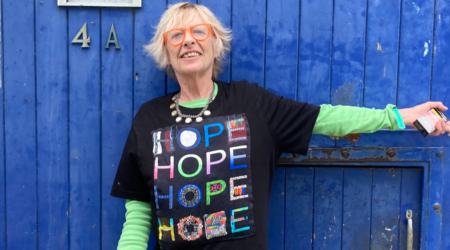 A photo of Jane Travers standing against a blue door wearing a t-shirt with the word hope repeated