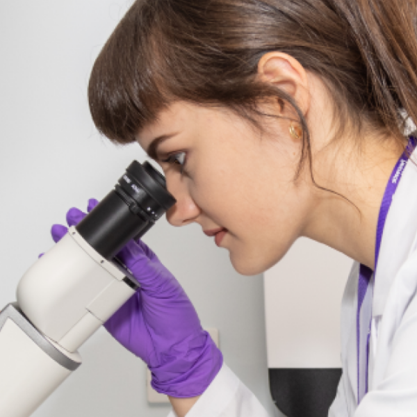 A researcher in a white lab coat looks down a microscope