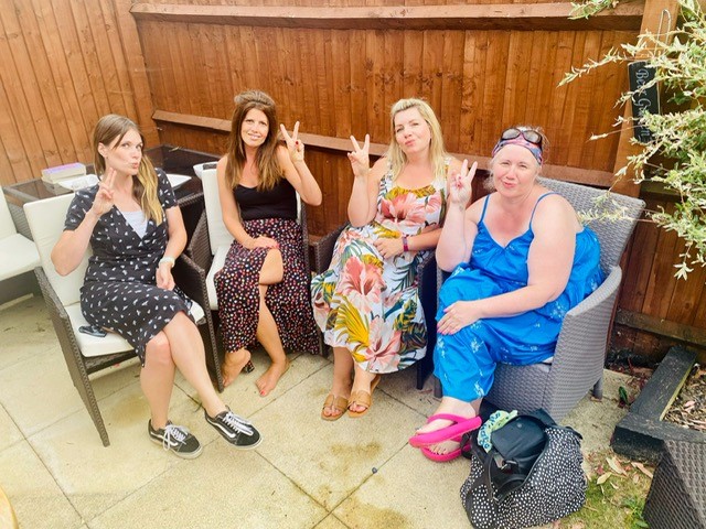 Friend sit next to Becki on chairs outside on a patio. They are all doing peace signs with their hands.