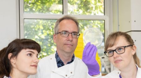 Scientist Professor Robin Ketteler standing in a lab with two of his colleagues looking at a sample