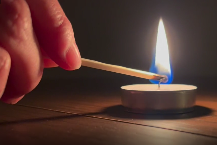 Light a candle in memory - a hand lighting a candle with a match