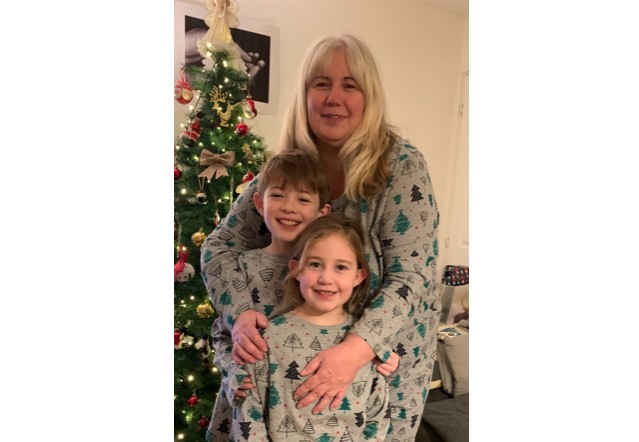 Becki stands with her arms around her children, Jacob and Georgie. They are in front of a Christmas Tree, on Christmas Day, in matching pyjamas