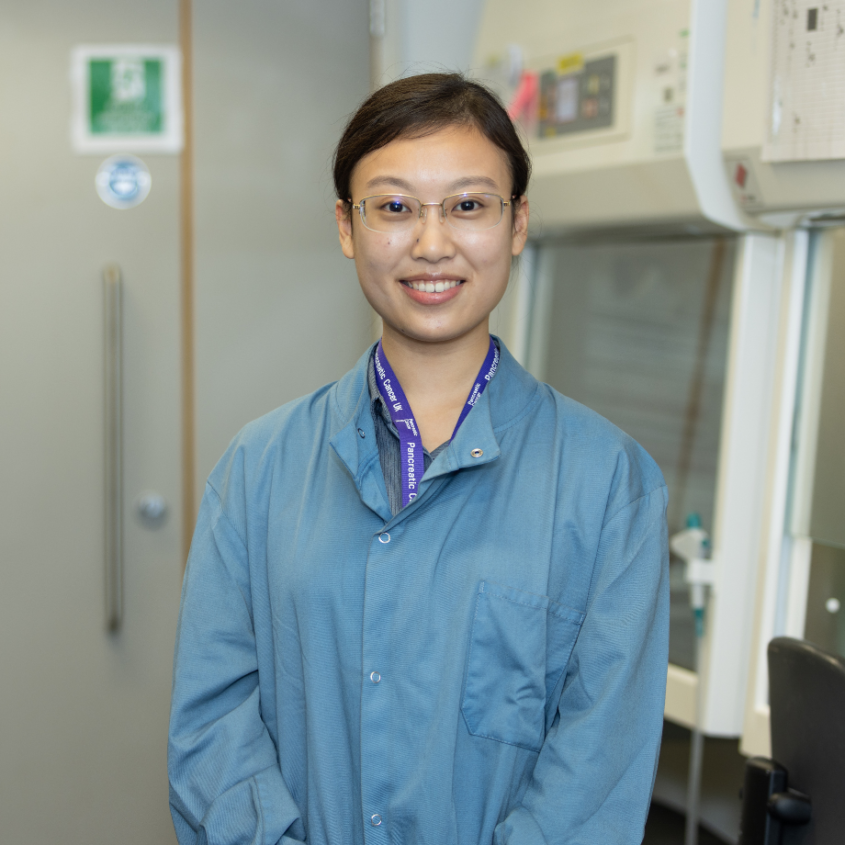 A woman standing in a lab coat in a research lab - PCUK