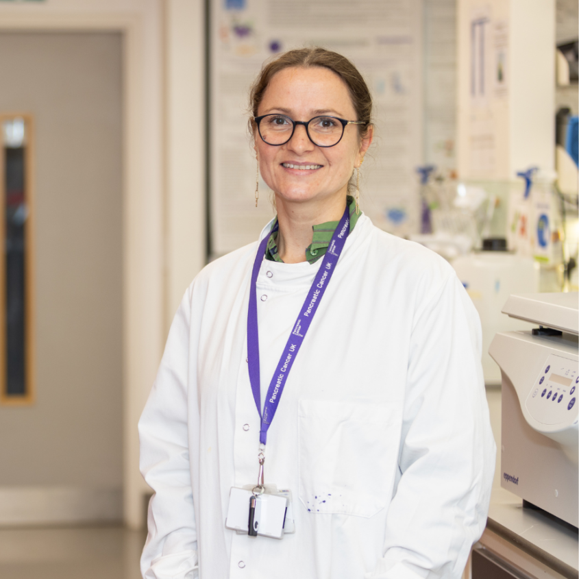 A woman standing in a lab coat in a research lab - PCUK - Stela