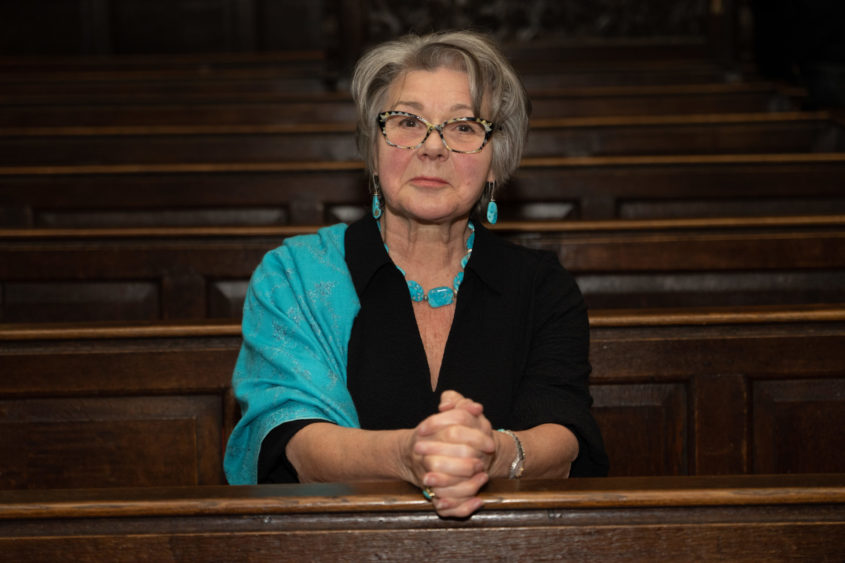 Actor Barbara Flynn sits on a pew wearing a turquoise shawl prior to our Carol Concert