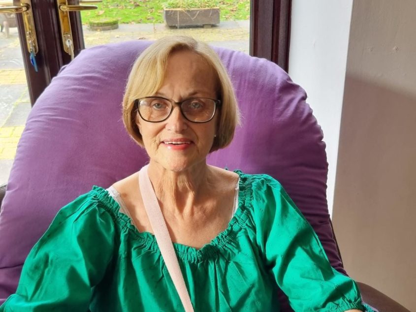 A woman dressed smartly in emerald green sits in a purple chemotherapy chair