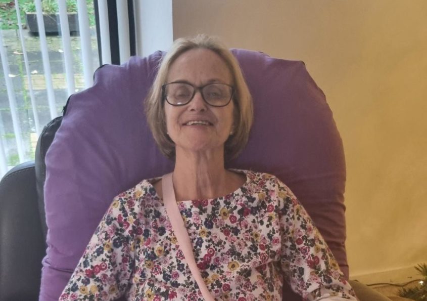 An older-looking woman in a chemotherapy chair, with a hand-made patchwork quilt on her knee.