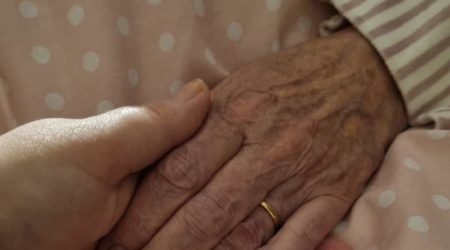 A young woman's hand gently holds the hand of an older woman