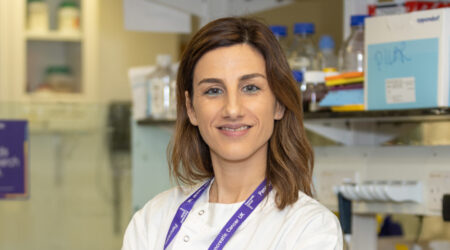 A female researcher wearing a lab coat with her arms folded, facing the camera