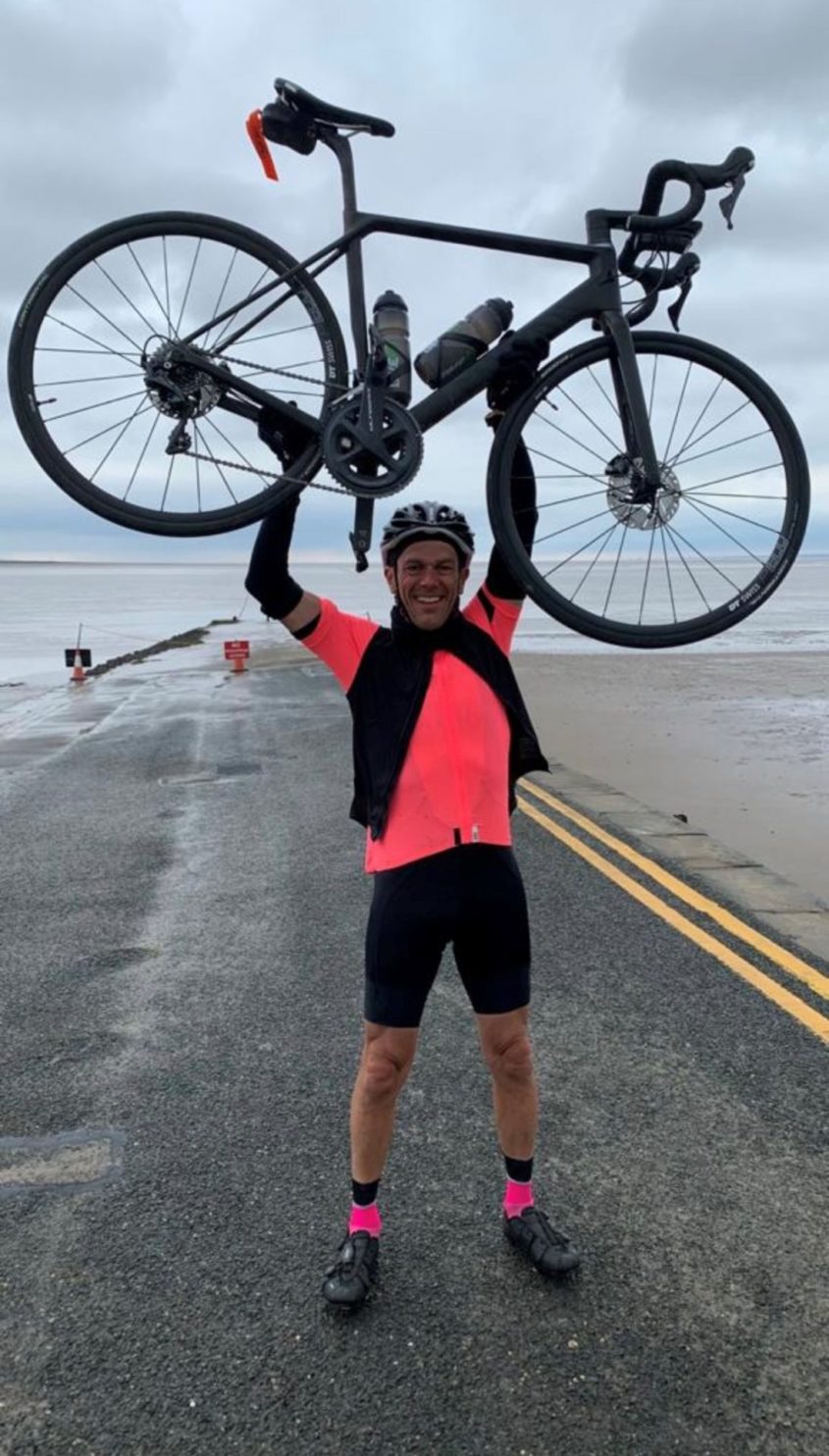 Man standing on a road and holding bike high above his head - Phil