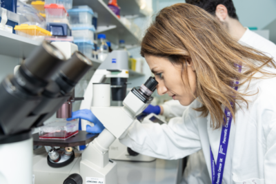 A female researcher wearing a lab coat looking down a microscope